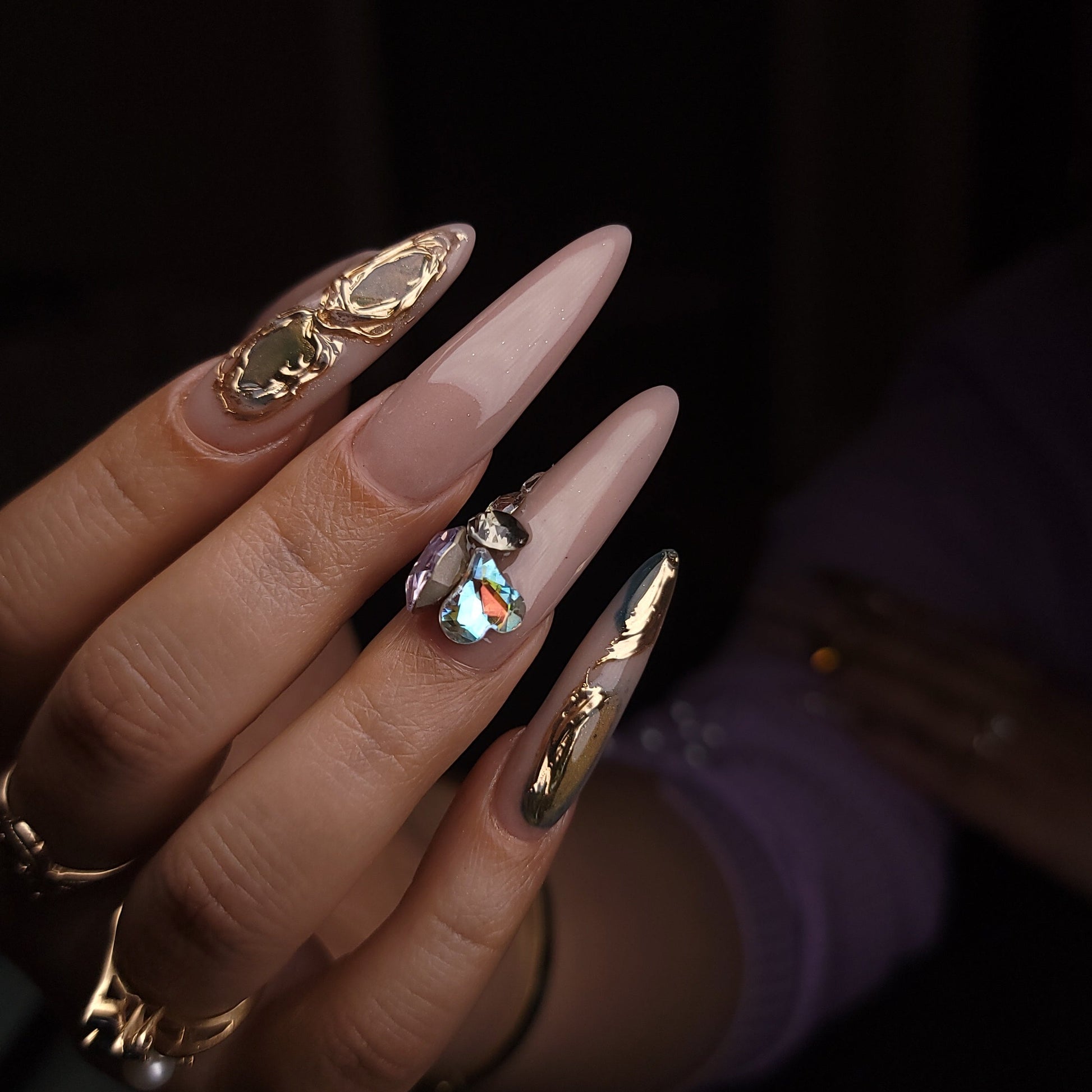 Close-up of a hand with long, pointed nails wearing multiple rings on a dark background